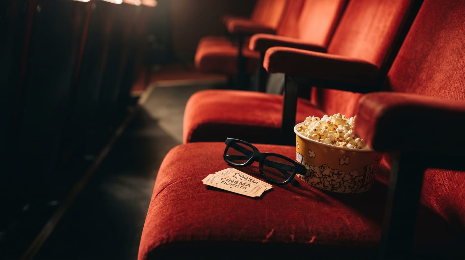 Bilete de cinema, ochelari 3D și un bol de popcorn pe un fundal roșu de sală de cinema