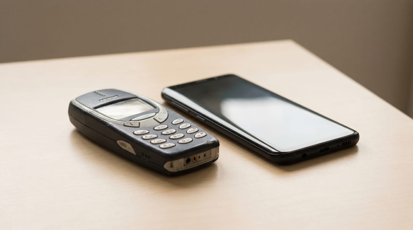 Telefon Nokia clasic cu taste, așezat lângă un smartphone modern, pe un fundal minimalist